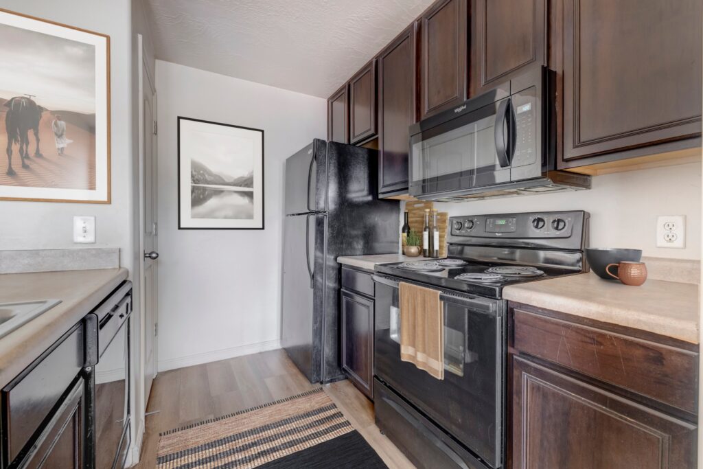 A modern kitchen with dark cabinets, a light countertop, stainless steel appliances, a central island with barstools, and bright natural light.